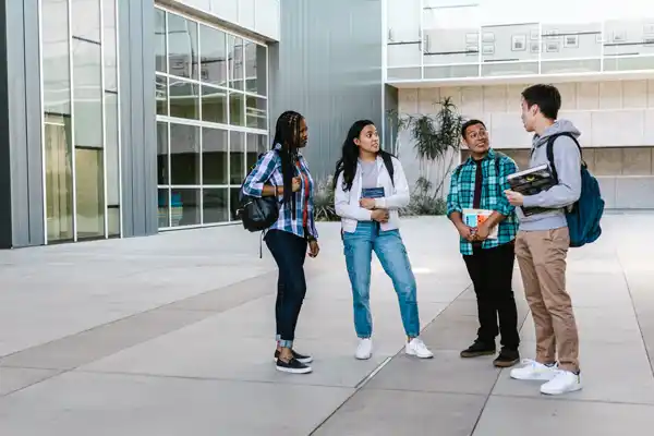 A diverse group of college students chatting outside a modern university building. (Image: RDNE Stock Project via Pexels.com)